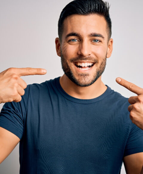 smiling man pointing to his white teeth 