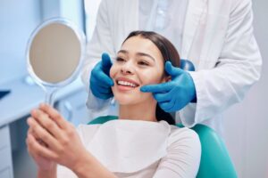 woman smiling into a mirror in the dental chair after a smile makeover